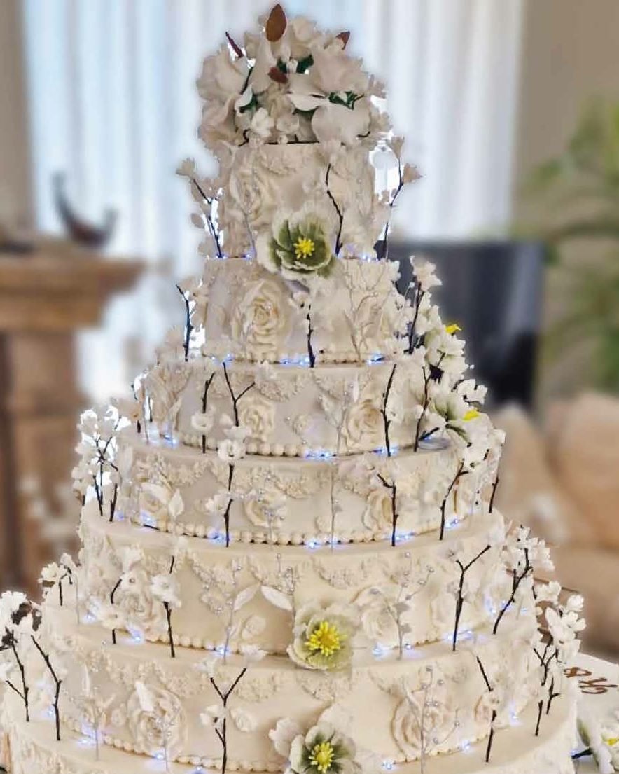 Tarta de boda blanca de varios pisos con flores y luces en Marbella
